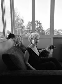 Side view of woman looking up while sitting with dogs on sofa at home