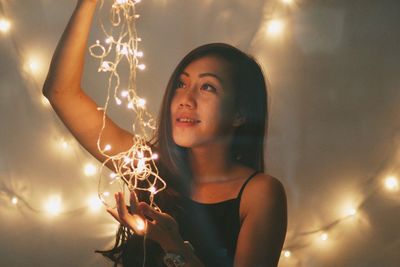 Close-up of young woman holding illuminated light bulb