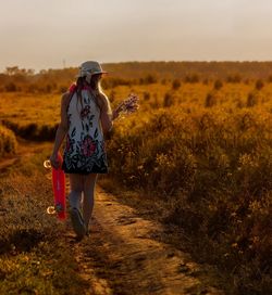 Rear view of woman walking on field against sky