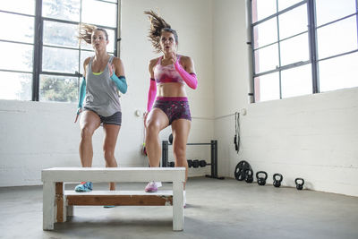 Female athletes exercising over wooden seat in gym