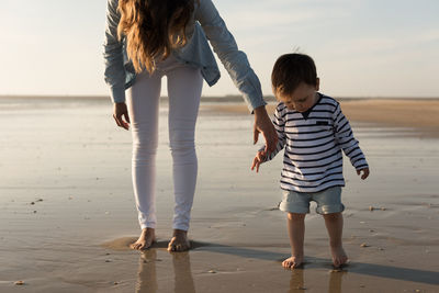Low section of mother with son walking at beach