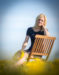 Portrait of young woman holding floral crown while sitting on chair at dandelion meadow