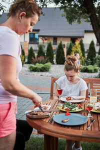 Family having a meal from grill during summer picnic outdoor dinner in a home garden