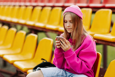 A teenage girl sits on the school bleachers and writes a message on her phone in her free time