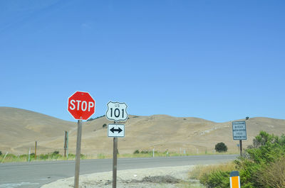 Road signs on landscape against clear blue sky