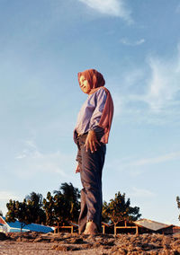 A girl is standing on the beach against the background of buildings, trees, clouds and sky