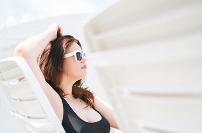 Stylish woman plus size body positive in black swimsuit and sunglasses on beach lounger near pool