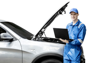 Portrait of male mechanic using laptop with car against white background