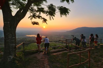 People standing by railing against sky during sunset