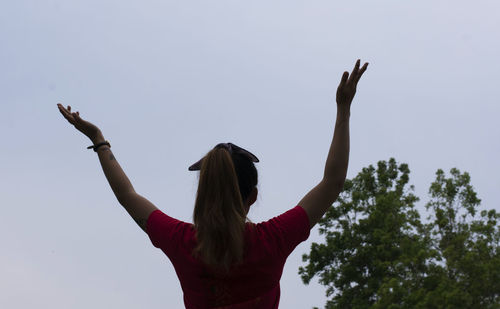 Rear view of woman with arms raised standing against clear sky