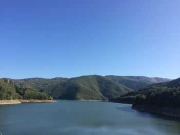 Scenic view of lake and mountains against clear blue sky