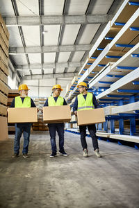 Three workers carrying boxes in factory warehouse