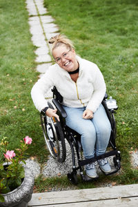 Full length portrait of smiling disabled woman sitting on wheelchair in backyard