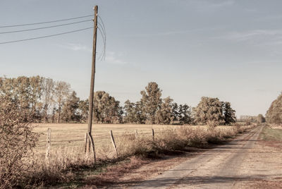 Dirt road amidst field against sky