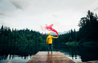 Rear view of man standing by lake against sky