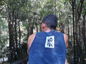 Rear view of man standing amidst trees in forest