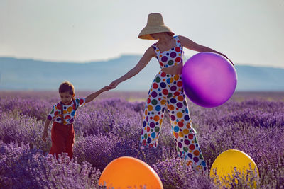 Woman in suit with multicolored polka dots ,hat in lavender field with child in multicolored costume