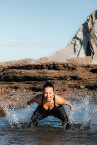 Portrait of woman in water splashing against sky