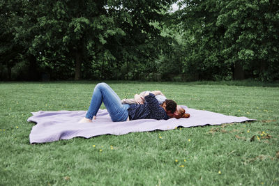 Mother embracing son while lying on picnic blanket at park