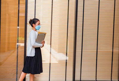 Side view of businesswoman holding laptop against wall