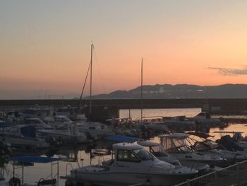 Boats moored at harbor against clear sky during sunset