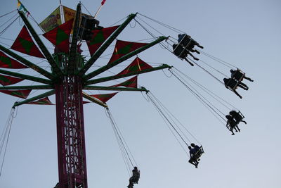 Low angle view of people on chain swing ride against clear sky