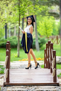 Portrait of smiling young woman with certificate standing on footbridge 