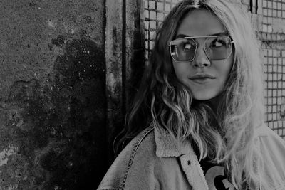 Portrait of woman wearing sunglasses against wall