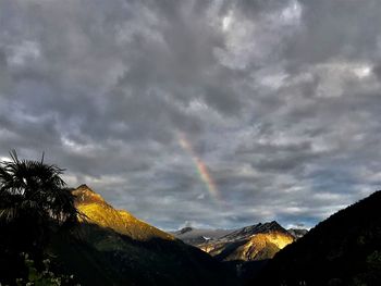 Scenic view of rainbow over mountains against cloudy sky