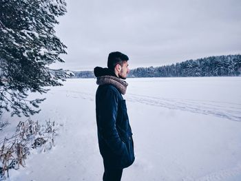 Side view of man standing on snow covered field against sky