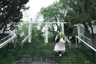 Rear view of woman on staircase against trees