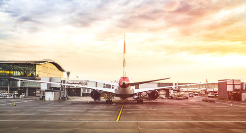 Airplane at airport runway against sky during sunset