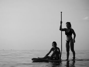 2 young women paddle boarding on sea against clear sky