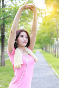 Woman listening music while stretching hands on footpath against trees
