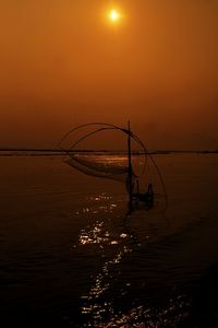 Silhouette fishing net on sea against sky during sunset