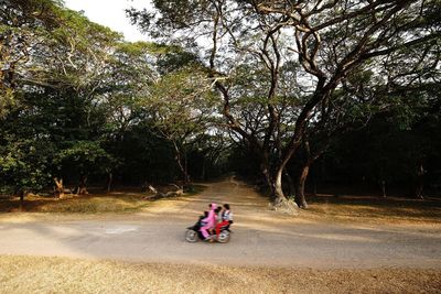 People riding motor scooter on street against trees