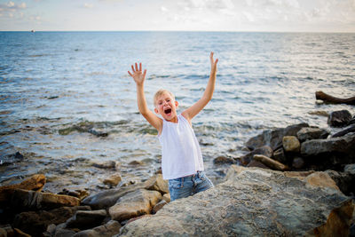 Boy standing on rock at beach against sky