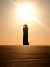 Lighthouse on beach against sky during sunset