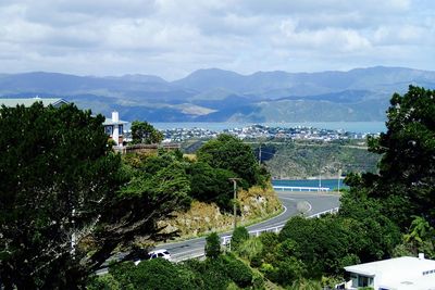 Road along trees with lake against mountain range in distance