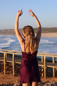 Rear view of woman standing at beach against sky