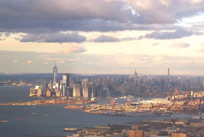 Modern cityscape by sea against sky during sunset