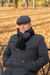 Portrait of smiling mature man sitting on bench at park during autumn