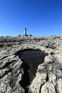 Lighthouse on rock by building against clear blue sky