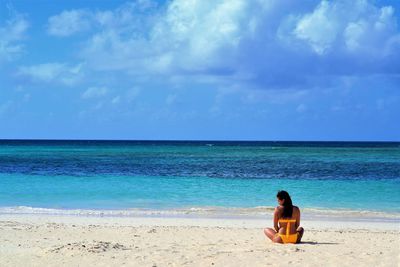 Man sitting on beach looking at sea against sky