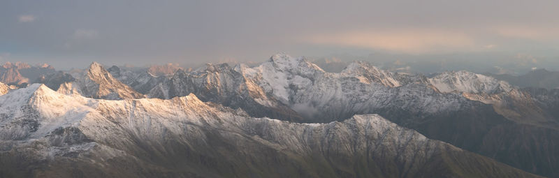 Panoramic shot of snowy mountain range with high peaks during orange sunset, austrian alps, europe