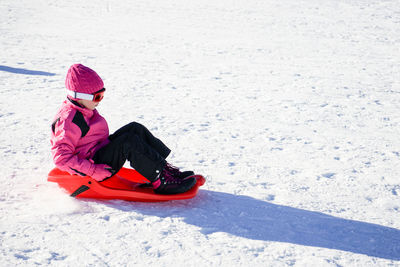 Girl sitting on sledge over snow covered land