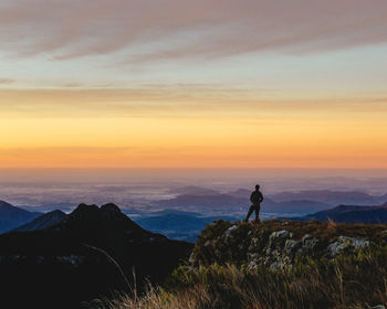 Silhouette man standing on mountain against sky during sunset