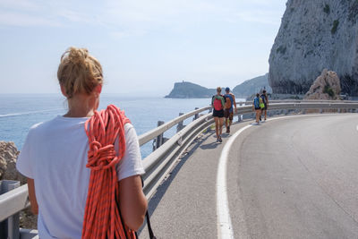 Rear view of people walking on road by sea against sky