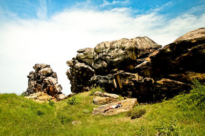 Female hiker relaxing on rock formation against sky during sunny day