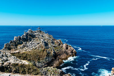 Scenic view of rocks in sea against clear blue sky